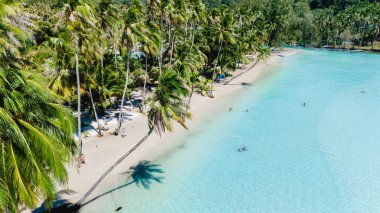 Yumuşak dalgalar Koh Kood kıyılarına vurur, palmiye ağaçları ılık esintide hafifçe sallanır. Ziyaretçiler şemsiyelerin altında dinlenirken canlı turkuaz suların ve güneşli kumların tadını çıkarıyorlar..