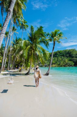 Bir kadın, parlak mavi gökyüzünün altında sallanan palmiyeler ve kristal berrak sularla çevrili Koh Kood 'un pitoresk plajlarında geziniyor ve huzurlu bir tropikal kaçışın tadını çıkarıyor..