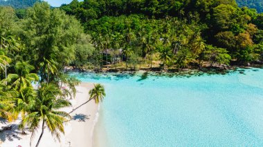 Sakin bir sahil, Tayland 'ın Koh Kood şehrinde yemyeşil yemyeşil ile çevrili yumuşak beyaz kumları gözler önüne seriyor. Sıcak güneşin altında hafif dalgalar kıyıya vurur, rahatlamak için mükemmel bir yer yaratır..