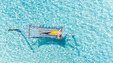 Bir kadın, kristal berrak turkuaz suların üzerinde asılı olarak, Koh KSemûd 'un doğal güzelliğiyle barışçıl bir biçimde hamakta. Güneş ışığı, suda parıldayan yansımalar yaratır..