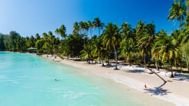 Kristal berrak sular, Tayland, Koh Kood 'un el değmemiş kıyılarına nazikçe çarpar. Bereketli palmiyeler sallanıyor tropikal esintide plaja gidenler güneşlenirken ve sakin atmosferin tadını çıkarırken.