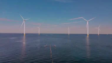 Nefes kesici bir panorama, Hollanda 'nın sakin sularında dimdik duran rüzgar türbinlerini sergiliyor. Okyanustaki yel değirmeni parkı, yel değirmeni türbinlerinin yeşil enerji üreten hava aracı görüntüsü.