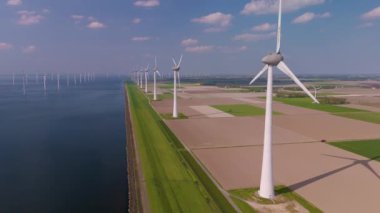 Hafif meltemler, huzurlu Hollanda manzarası boyunca zarifçe dönen devasa yel değirmeni türbinlerine rehberlik eder. Bu çarpıcı manzara doğanın ve yenilenebilir enerjinin uyumunu vurgular..