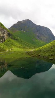 Bereketli yeşil tepeler, bulutlu bir gökyüzünün altında mükemmel bir şekilde yansıyan, sakin bir gölü beşiyorlar. Bu el değmemiş manzara Norveç 'in doğal güzelliğini ve huzurunu gözler önüne seriyor..