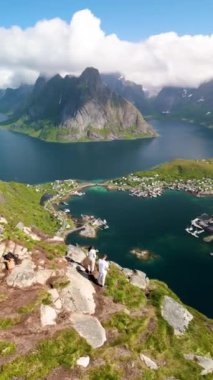 Norveç 'te nefes kesen manzaraları keşfedin. İki maceracı kayalık bir tepenin tepesinde, büyüleyici kıyı köyleri ve dağlarla kaplı sakin bir körfeze bakıyor. Reinebringen yürüyüşü Lofoten Norveç