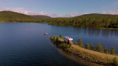 Norveç 'in nefes kesici güzelliğini keşfedin. Bereketli yeşilliklerle çevrili sakin bir gölün yanında bir karavan duruyor. Sakin sularda süzülen bir tekne çarpıcı manzarayı ve huzurlu geri çekilmeyi sergiliyor..