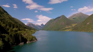 Norveç fiyortlarının doğal güzelliğini kristal berrak sularla, yüksek dağlarla ve canlı yeşilliklerle tecrübe edin. Doğa, sıcak güneşin altında huzur dolu bir atmosfer yaratarak gelişiyor..