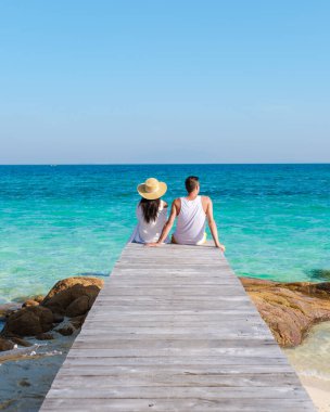Berrak sularda huzurlu bir anın tadını çıkaran bir çift, Tayland 'ın Rayong kentindeki Koh Munnork Adası' nın güzelliğiyle çevrili ahşap bir rıhtımda, parlak bir gökyüzünün altında dinleniyor..