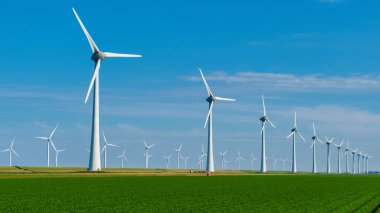 Rüzgar türbinleri, Hollanda 'nın yemyeşil alanları arasında yenilenebilir enerji üreten canlı bir gökyüzüne karşı duruyor. Yel değirmeni türbinleri Noordoostpolder enerji geçişi için yeşil enerji yaratıyor