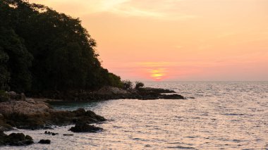 Güneş Koh Munnork Adası 'nın sakin sularında batarken gökyüzünü altın renkleri kaplıyor. Yeşillik kıyı şeridini çevreleyerek doğa severler için barışçıl bir kaçış sağlıyor..