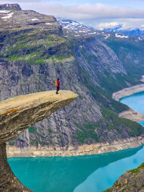 Yalnız bir maceracı, ikonik Trolltunga 'nın tepesinde duruyor. Norveç' te yaz aylarında dramatik bir gökyüzünün altında büyüleyici fiyortlara ve kar örtülü zirvelere bakıyor.