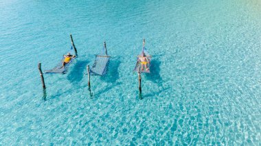 Güneş banyosu, Tayland, Koh Kood 'un el değmemiş sularındaki sıcak tropikal güneşin tadını çıkararak yüzen hamaklarda dinlenir. Bir çift erkek ve kadın okyanusun yukarısındaki bir hamakta dinleniyorlar.