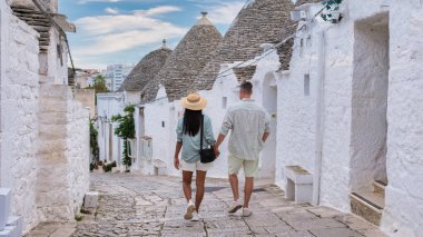 Bir çift el ele yürür Alberobello Puglia 'nın beyaz yıkamalı caddelerinde, İtalya' da, eşsiz trulli binalarla çevrili, çeşitli erkek ve kadınlar tatilde.