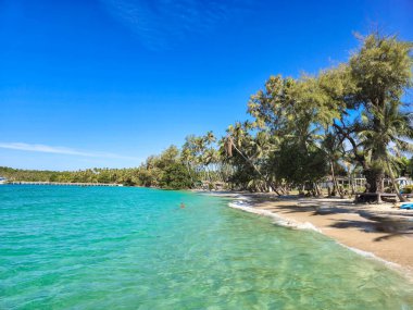 Bereketli palmiye ağaçları kumlu sahil boyunca yavaşça sallanırken, parlak mavi sular parlak güneşi yansıtıyor. Ziyaretçiler, Koh Kood, Tayland 'ın huzurlu atmosferi ve manzarasının keyfini çıkarıyorlar..
