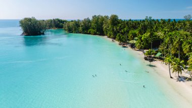 Yumuşak dalgalar kıyıya vururken güneş tarafından öpülen kumsalcılar Koh Kood 'un canlı turkuaz sularının tadını çıkarıyorlar. Palmiyeler nazikçe sallanıyor, Tayland 'ın bu kesimini çerçeveliyor sakin kıyı şeridini.
