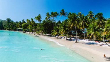 Koh Kood 'un turkuaz sularında güneş ışığı dans ediyor, ziyaretçilerin dinlendiği ve cennetin sıcacık kucaklamasının keyfini çıkardıkları palmiye püsküllü plajları aydınlatıyor..