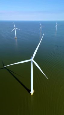 Uzun rüzgar türbinleri, Hollanda 'nın sakin sularının üzerindeki serin meltemde zarifçe döner. Okyanustaki yel değirmeni parkı, yel değirmeni türbinlerinin yeşil enerji üreten hava aracı görüntüsü.