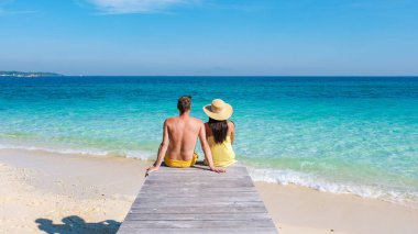 Bir çift erkek ve kadın, Koh Munnork Adası 'nın çarpıcı turkuaz sularını içlerine çekerek ahşap iskelede dinleniyorlar. Parlak güneş, huzurlu bir kaçış için mükemmel sakin atmosferi yükseltir..