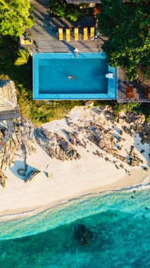 Bir Tayland adasının sakin manzarası turkuaz denize bakan güzel bir yüzme havuzunu gözler önüne serer. Güneş pansiyonları kumlu sahilde rahatlamayı bekliyor, mükemmel bir tropikal kaçış yaratıyorlar..