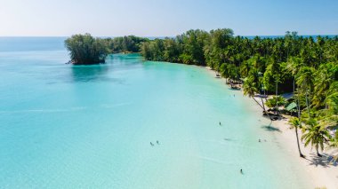 Yumuşak dalgalar kıyıya vururken ziyaretçiler bereketli yeşilliklerle çevrili Koh Kood 'un büyüleyici turkuaz sularının tadını çıkarıyorlar. Güneş ışığı yüzeyde ışıldar, rahatlatır..