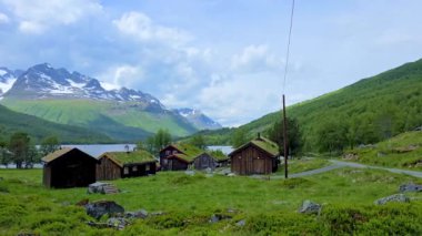 Norveç 'in dingin, yemyeşil, sakin bir gölün kıyısına kurulmuş güzelliğini hissedin. Tuhaf ahşap kulübeler, berrak mavi gökyüzünün altında görkemli dağlarla uyum içinde.