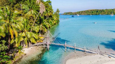 Tayland 'daki Koh Kood' un güzelliğini keşfedin, büyüleyici bir tahta köprü kumlu kıyıları birbirine bağlar. Bereketli palmiye ağaçları, güneş sakin suların üzerinde yavaşça süzülür ve resim gibi bir manzara çizer..