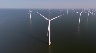 Dev rüzgar türbinleri Hollanda 'nın sakin suları üzerinde zarifçe dönerek rüzgarın enerjisini yakalıyor. Okyanustaki yel değirmeni parkı, yel değirmeni türbinlerinin yeşil enerji üreten hava aracı görüntüsü.