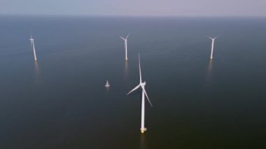 Hollanda 'nın sakin sularına karşı dimdik duran yel değirmeni türbinlerinin zarafetine tanık olun. Yelkenliler süzülüyor, yenilenebilir enerji ve doğanın uyumunu somutlaştırıyor..