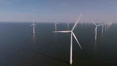 Hollanda 'daki mavi gökyüzüne karşı dimdik duran rüzgar türbinlerinin nefes kesici manzarası. Okyanustaki yel değirmeni parkı, yel değirmeni türbinlerinin yeşil enerji üreten hava aracı görüntüsü.
