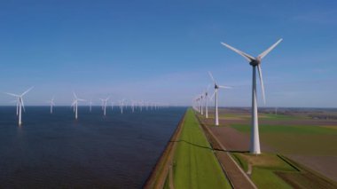 Yükselen yel değirmeni türbinleri Hollanda 'nın pitoresk kıyı şeridi boyunca uzanır, yenilenebilir enerjiyi kullanırken okyanusun geniş mavi gökyüzü ve sakin sularıyla güzelce harmanlanır..