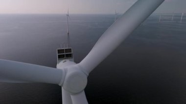 Hollanda 'nın mavi ufkunda dimdik duran etkileyici rüzgar türbinleri üzerinde süzülür. Okyanustaki yel değirmeni parkı, yeşil enerji üreten yel değirmeni türbinlerinin drone hava görüntüsü. 