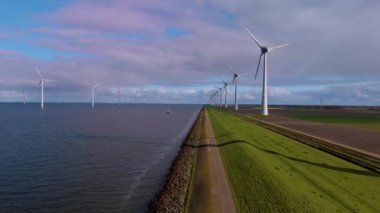 Uzun yel değirmeni türbinleri Hollanda kıyı şeridi boyunca zarifçe dönerek rüzgarın gücünü sürdürülebilir enerji için kullanırlar. Huzurlu manzara doğa ve teknolojinin bir karışımını sergiliyor. 
