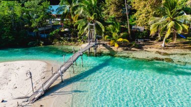 Koh Kood, Tayland 'da, bereketli palmiyeler ve kumlu kıyılarla çevrili, parlak mavi gökyüzü altında rahatlama ve keşifleri davet eden, büyüleyici, ahşap bir köprü berrak suları kaplar..