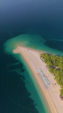 Hırvatistan 'da kristal berrak sular ve yemyeşil sularla çevrili muhteşem kumlu bir plajın dinginliğini hissedin. Renkli şemsiyeler altında gevşeyin ve Brac Hırvatistan 'daki Zlatni Rat plajının tadını çıkarın.