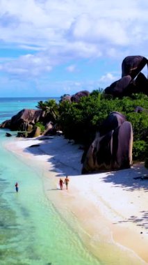 Anse Kaynağı DArgent La Digue Seyşeller, parlak mavi bir gökyüzü altında, çarpan granit kayalar ve yemyeşil yeşilliklerle çevrili, el değmemiş sahil boyunca yürürler..