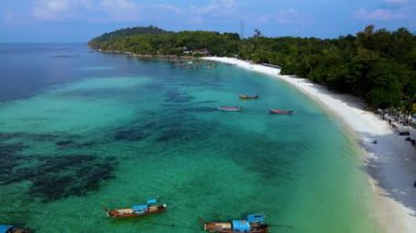 Canlı teknelerin turkuaz sularda dinlendiği Tayland 'daki Koh Lipe' nin el değmemiş kıyılarını deneyin. Parlak mavi gökyüzünün altındaki sakin kumsalı ve yemyeşil çevreyi keşfedin..