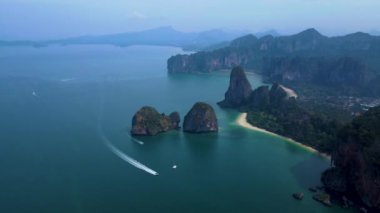 Zümrüt sularının görkemli kayalıklarla buluştuğu Krabi Tayland 'ın nefes kesici güzelliğini keşfedin. Huzurlu körfezde yelken açarken canlı günbatımı renkleri manzarayı aydınlatıyor..