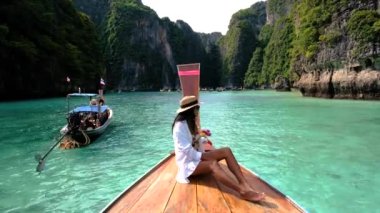 Bir kadın teknede dinlenirken Krabi Tayland 'ın çarpıcı turkuaz sularını tecrübe edin. Etrafı yüksek uçurumlar ve yemyeşil ağaçlarla çevrili Koh Phi Adası.