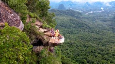 İki macera meraklısı Tayland, Krabi 'de nefes kesici bir uçurumun kenarında oturmuş aşağıdaki genişleyen orman manzarasına hayret ediyorlar. Khao Ngon Nak