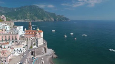 Sıcak güneş ışığı, renkli binaların kristal berrak sularla buluştuğu Amalfi kıyı köyünü yıkıyor. Bereketli dağların çerçevelediği sakin körfezde gezinen tekneler güzel bir kaçış yolu yaratıyor..