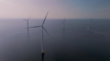 Görkemli yel değirmeni türbinleri Hollanda kıyı şeridinin sakin zeminine karşı dik dururlar. Bu büyüleyici görüntü sürdürülebilir enerjiyi eylem halinde gösteriyor, doğayla uyum içinde..