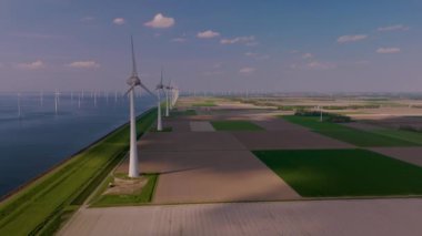 Görkemli yel değirmeni türbinleri Hollanda 'nın düz arazilerini süsleyerek rüzgâr enerjisini mavi gökyüzü ve sakin sulara karşı kullanıyor. Doğa ve teknoloji uyum içinde birleşir..