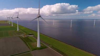 Yükselen yel değirmeni türbinleri Hollanda 'nın sakin kıyı şeridi boyunca zarifçe dönüyor. Bu çarpıcı manzara, sürdürülebilir bir geleceğe katkıda bulunurken yenilenebilir enerjinin güzelliğini gösteriyor..