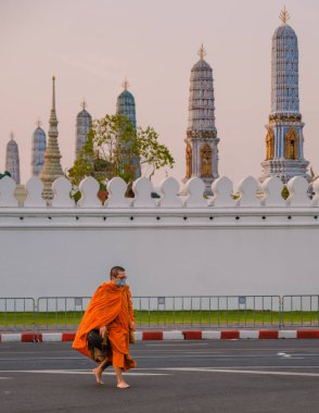 Bangkok Tayland 10 Ocak 2025 'te, parlak turuncu cüppeli bir keşiş Wat Phra Kaew' de, Grand Royal Palace 'ın doğu tarafında, sessiz bir cadde boyunca yalınayak yürür.