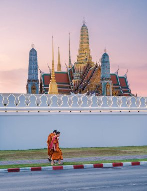 10 Ocak 2025 'te Bangkok Tayland' da, canlı cübbeler içindeki keşişler sokakta zarif bir şekilde yürürken, muhteşem Grand Palace arka planda sakin bir sabah erken saatlerde yükseldi..