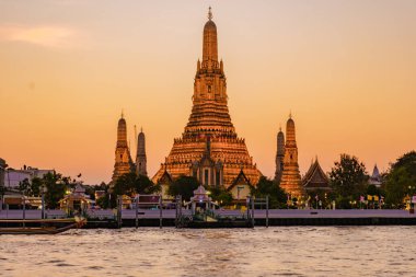 Altın ışık, şafak tapınağı Wat Arun 'u yıkıyor. Alacakaranlık Bangkok' a inerken. Görkemli kuleler nehri zarif bir şekilde yansıtıyor ve akşam yürüyüşleri için sakin bir atmosfer yaratıyor..