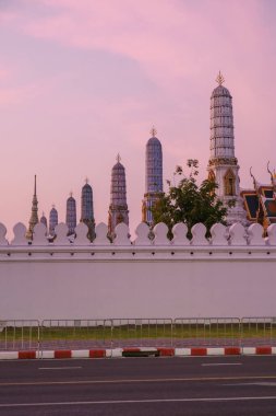 Majestic temple spires reach towards a pastel sky as dusk settles over Bangkok. The intricate architecture contrasts with the peaceful urban landscape, Grand palace Bangkok Thailand clipart