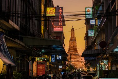 10 Ocak 2025 'te Bangkok Tayland' da, gün batımında Bangkok 'un hareketli caddelerinin üzerindeki Wat Arun kulelerinin büyüleyici silueti. Renkli işaretler geceyi aydınlatıyor, canlı bir atmosfer yaratıyor. 