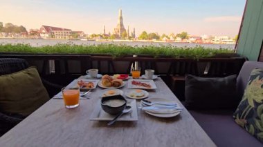 Nefesimi kesen nehir manzarasının tadını çıkarırken taze meyve, pasta ve içeceklerle nefis bir kahvaltı yapın. Nehre ve Wat Arun 'a bakan dingin atmosferin ve canlı manzaranın tadını çıkar.