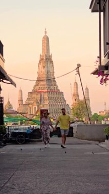 Bir çift, Wat Arun yakınlarındaki Alacakaranlık büyüsünü yakalamak için Bangkok 'un büyüleyici sokaklarında el ele yürür. Tapınağın çarpıcı mimarisi renkli gökyüzüne karşı dimdik ayakta duruyor..